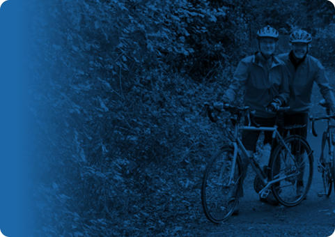 Blue banner with a photo overlayed that shows two middle-aged men standing next to their bikes on an outdoor trail.